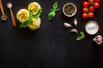 Fettuccine with ingredients for cooking pasta - tomatoes and basil with garlic - on a black background, top view. Flat lay