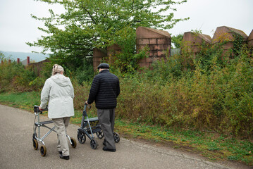 Elderly people taking a walk with help of walker with friends on a cold day through the park