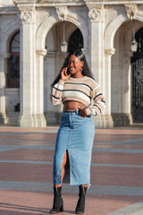 Fototapeta premium Young black woman smiling and talking on smartphone in urban setting, having conversation, making phone call, connecting with friends and family, modern communication