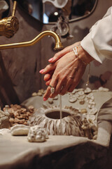 Young woman washes hands in seashell-decorated basin while wearing fashionable pearl beads