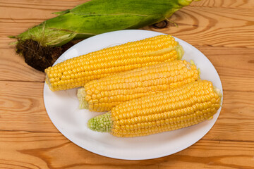 Peeled raw sweet corn ears on dish against unpeeled ear