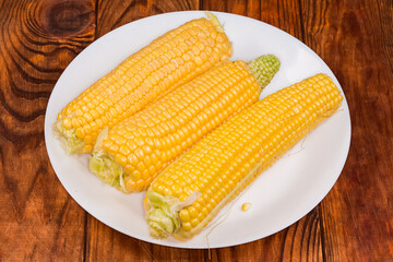 Peeled raw sweet corn ears on dish on rustic table
