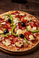 Pizza with chorizo ​​sausage, mozzarella cheese, green pepper and black olives. Rustic wooden background. Soft focus.	
