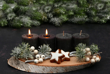 Arrangement for the second Advent with text space: Natural Advent decoration with brown candles, cinnamon stars and fir branches in the background.