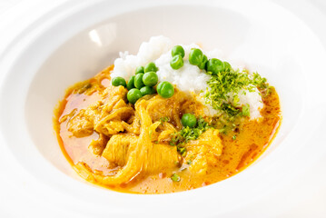 Indian chicken curry with white rice and green peas, served in a white bowl. Traditional spicy dish with vibrant colors, garnished with herbs. Top view, close-up