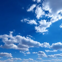 Obraz premium A bright, sunny day with puffy clouds floating across a clear, blue sky. The sky is filled with soft, fluffy cumulus clouds, creating a sense of peace and tranquility