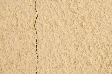 A sharp, dark crack runs down a bumpy, beige-colored stucco wall, effectively illustrating concepts of structural damage, wear and tear, and the need for inspection.