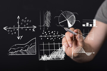 Stock photo of a hand drawing various business charts and graphs on a black background. Ideal for presentations, reports and marketing mat