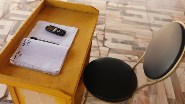 Yellow mobile money (MoMo) stand with notebook, pen, and basic phone. Fintech, digital payments and financial inclusion in Africa.