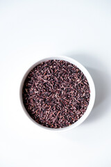 A bowl of black sticky rice grains isolated on white background