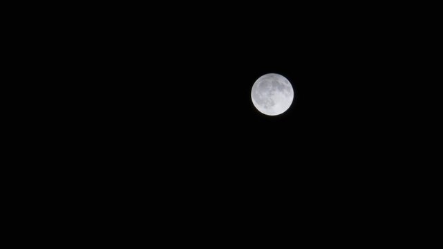 full moon slowly rising in a starless and cloudless night sky.