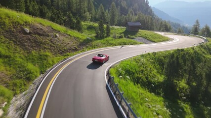 Drone view of a red supercar navigating a sharp mountain hairpin surrounded by greenery and alpine scenery. Category: Transportation