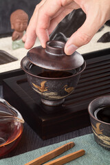 Tea ceremony in a gaiwan teapot on the tea table. A hand lifts the lid of a gaiwan.