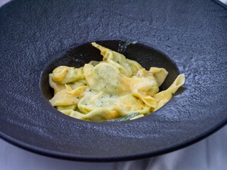 Deliciously prepared vegan tortelli stuffed pasta served in a rustic textured black bowl with a creamy herb sauce and scattered fresh herbs