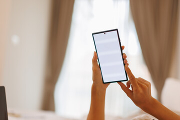 Asian woman hands using white smartphone with blank screen while lying in bed at morning
