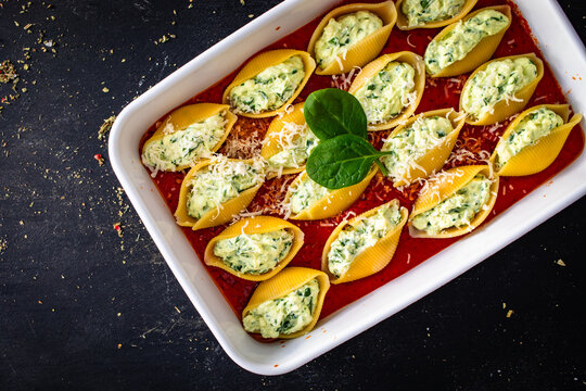 Pasta shells stuffed with cheese and spinach in tomato sauce in baking dish prepared for baking on black table