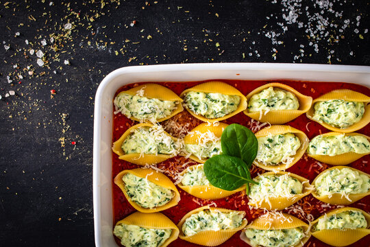 Pasta shells stuffed with cheese and spinach in tomato sauce in baking dish prepared for baking on black table