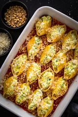 Pasta shells stuffed with cheese and spinach in tomato sauce in baking dish prepared for baking on black table