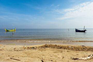 Fishing boats rest under a bright blue sky on a peaceful tropical beach. © Fais