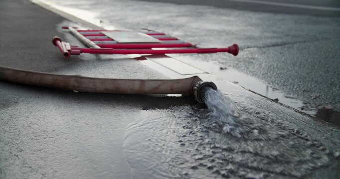 Close-up of water flowing from fire hose onto asphalt surface in urban street.