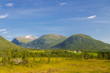 Fototapeta premium The amazing green meadows of the More and Romsdal county in Norway with in the backgroudn the massive rock formations and hills rising up from the ground and the imposing fjords.