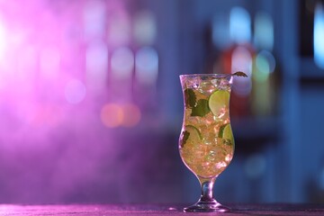 Glass of alcoholic cocktail on table against blurred background with smoke, space for text