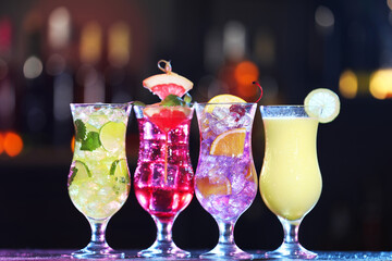 Glasses of alcoholic cocktails with garnish on table against blurred background
