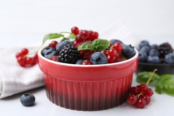 Different ripe berries and basil leaves in bowl on white table, closeup
