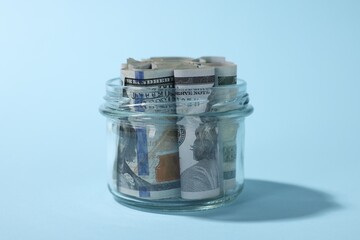 Glass jars with dollars on light blue background, closeup