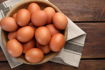 Raw chicken eggs in bowl on wooden table, top view. Space for text