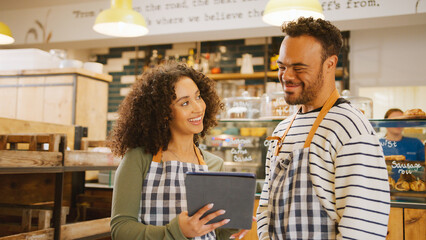 Woman Using Digital Tablet Working In Coffee Shop Training Man With Down Syndrome