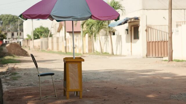 Mobile money (MoMo) stand with a colorful umbrella and chair on roadside in an urban area. Fintech, digital payments and financial inclusion in Africa.