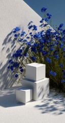 Three white cubic display objects are showcased against a backdrop of vibrant blue flowers and a textured white wall, creating a serene and aesthetically pleasing scene.