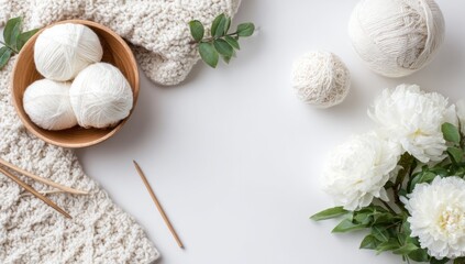 A serene overhead view of knitting supplies, yarn balls, and fresh white peonies, arranged on a bright white surface, showcasing a tranquil and artistic composition.