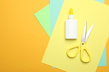 Glue, scissors and color paper on yellow background, flat lay. Space for text