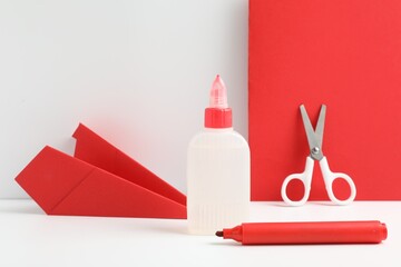 Glue, scissors, paper plane and marker on white table against color background