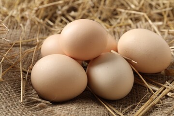Raw chicken eggs and straw on table, closeup