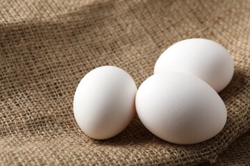 Raw chicken eggs on burlap cloth, closeup. Space for text
