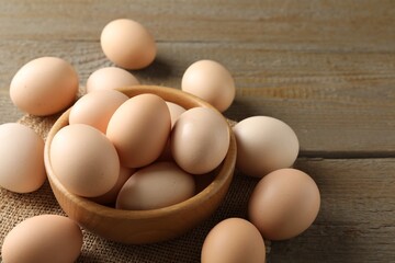 Raw chicken eggs in bowl on wooden table, closeup. Space for text