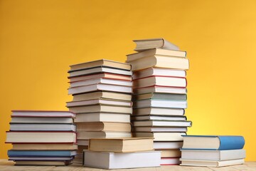 Many stacked books on table against yellow background