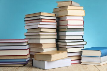 Many stacked books on wooden table against light blue background