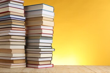 Many stacked books on table against yellow background. Space for text