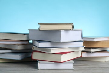 Many stacked books on wooden table against light blue background, closeup