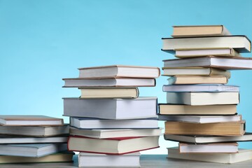 Many stacked books on wooden table against light blue background. Space for text