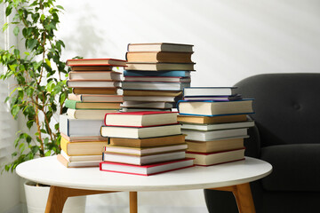 Many stacked books on white table and sofa indoors