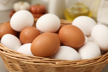 Raw chicken eggs in wicker basket on wooden counter indoors, closeup