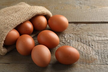 Raw chicken eggs in burlap sack on wooden table, closeup. Space for text