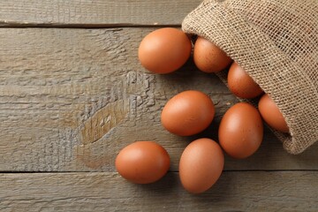 Raw chicken eggs in burlap sack on wooden table, flat lay. Space for text