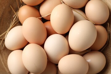 Raw chicken eggs and straw in bowl, top view