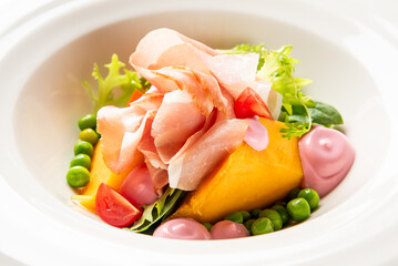 Gourmet salad with prosciutto, roasted squash, green peas, tomato, arugula, frisée, and pink sauce, artistically plated in a white bowl. Fine dining presentation, top view
